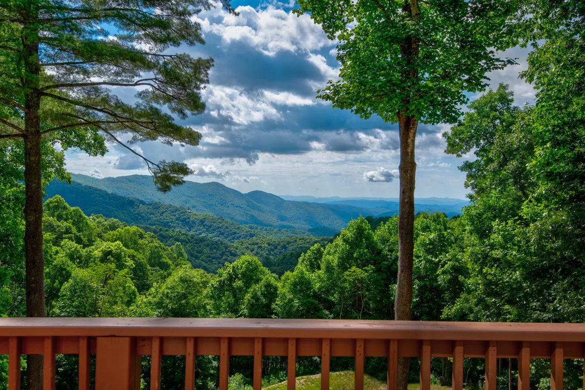 A breathtaking mountain view as seen from a wooden railing, with lush greenery, a dramatic sky, and distant ridges fading into the mist. The scene feels peaceful and expansive—perfect for enjoying a morning coffee, quiet reflection, or simply soaking in the surrounding beauty. The composition draws the eye toward the horizon, emphasizing the scenic aspect of the retreat.