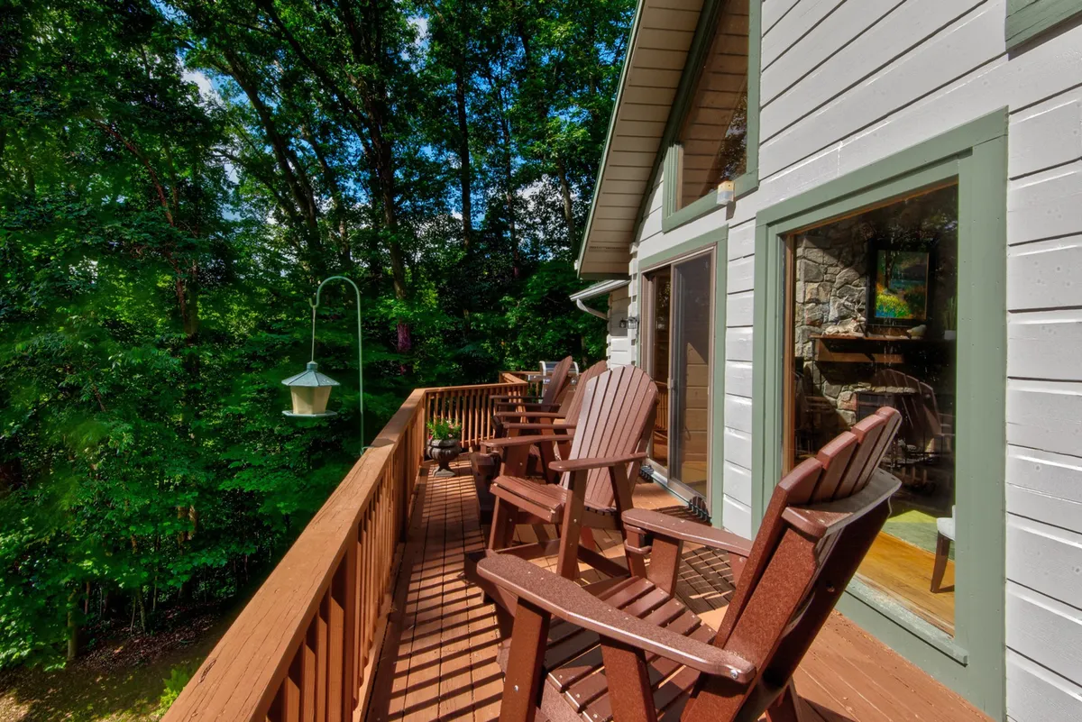 A serene wooden deck with Adirondack chairs is nestled among towering trees. A hanging lantern adds a rustic touch to this peaceful setting, which invites guests to relax, socialize, or watch for wildlife after a day spent on the trails.