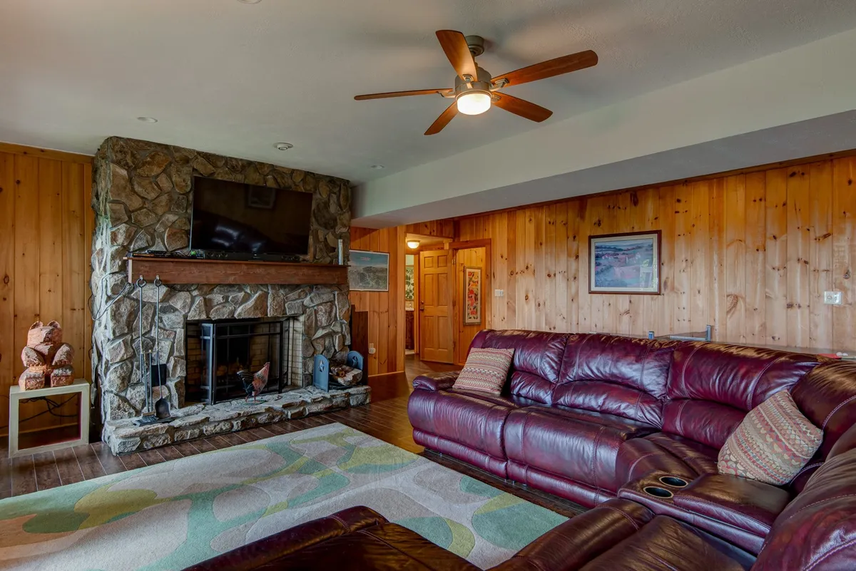 A warm, inviting room with a stone fireplace, leather sofa, wood paneling, and a TV. The setup is ideal for relaxing movie nights or gathering for family game sessions, exuding comfort and togetherness.