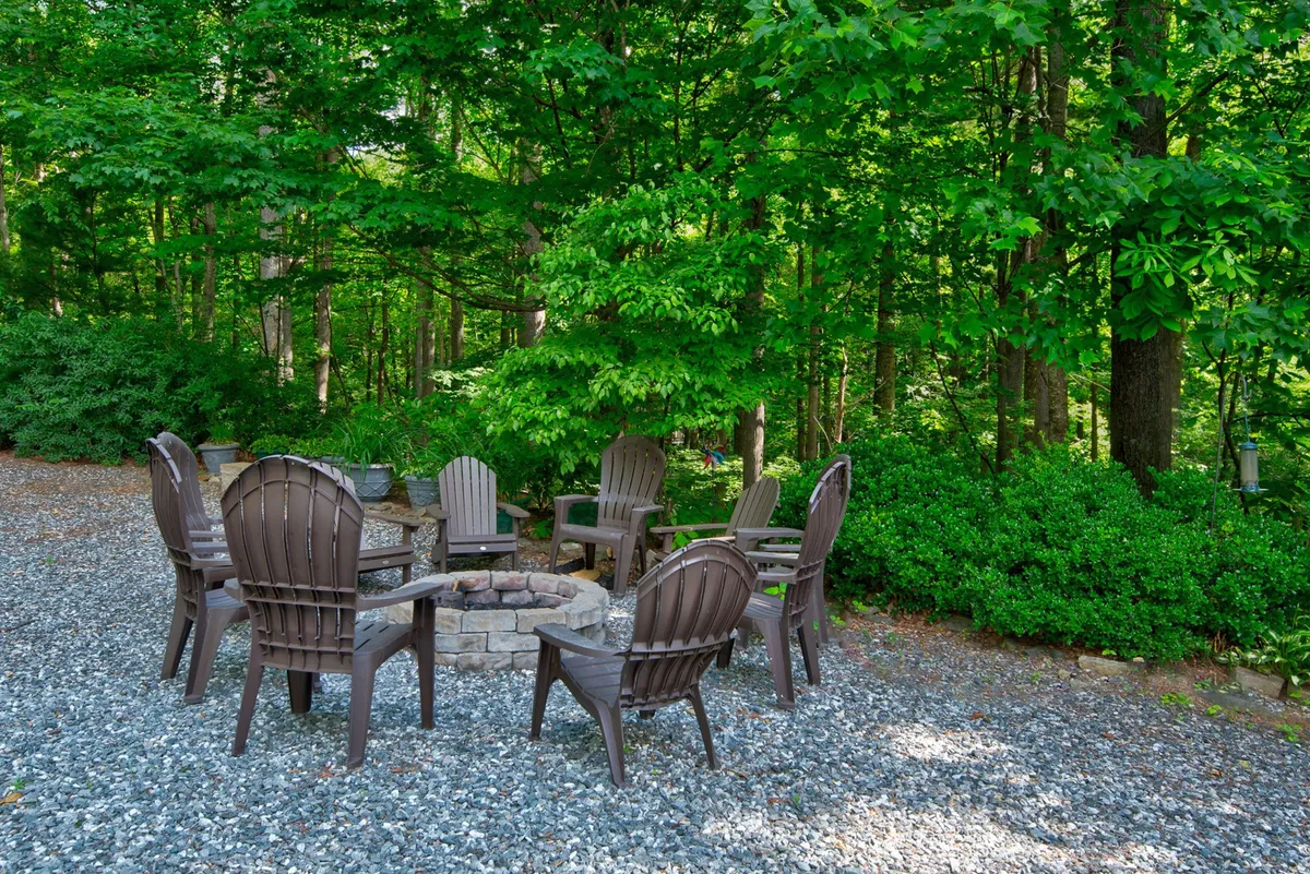 A cozy fire pit setup with Adirondack chairs arranged in a circle, surrounded by trees and greenery. The scene evokes warmth, camaraderie, and evenings spent sharing stories under the stars.