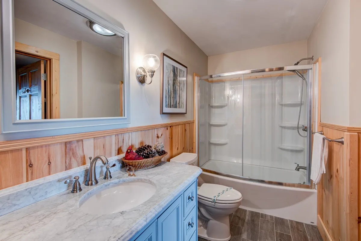 A stylish bathroom featuring a marble-topped vanity, a framed mirror, and a shower area adorned with wood paneling and decorative pinecones, evoking a spa-like, rejuvenating atmosphere.