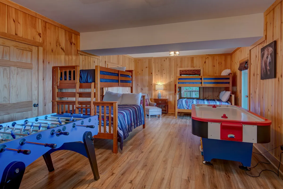 A vibrant bunk room equipped with bunk beds, a foosball table, air hockey table, and a cozy armchair. The room’s playful decor makes it ideal for kids or group stays, offering both sleeping space and entertainment.
