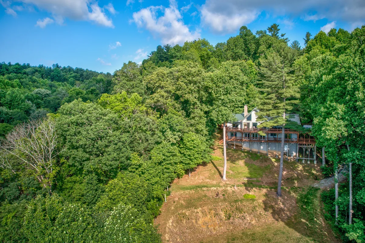 This image displays the house nestled among towering trees with a broad deck area, inviting relaxation and outdoor gatherings. The setting feels private and is enveloped in natural beauty, suggesting a peaceful, secluded environment ideal for unwinding or working remotely in tranquility.