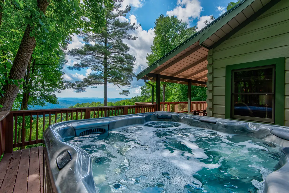 A serene hot tub set on the deck, offering unobstructed mountain views and encircled by tall trees. The scene is peaceful, inviting guests to unwind while soaking in the natural surroundings.