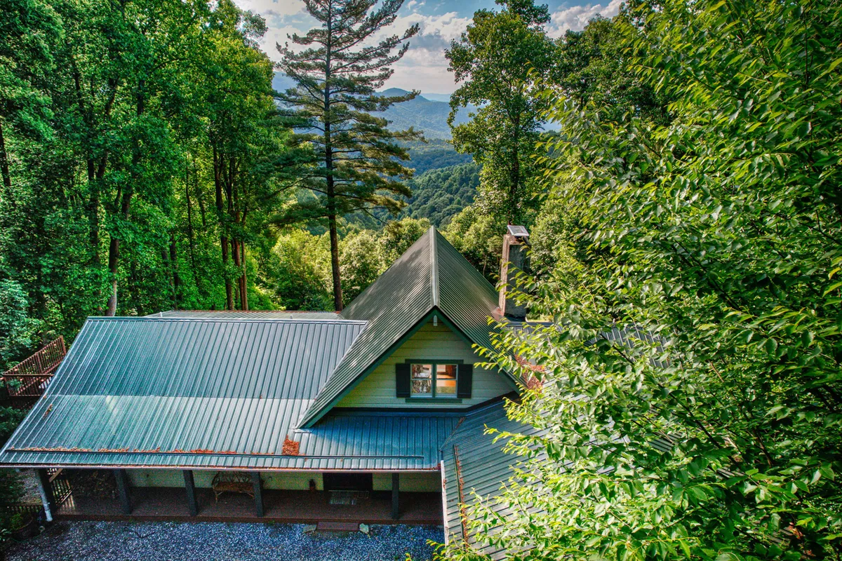 A wide exterior shot shows the house nestled amidst trees with a panoramic mountain view and a welcoming roofline. The natural setting hints at easy access to hiking trails and outdoor adventures, complementing the section's focus on exploration and proximity to the Blue Ridge Parkway and Mountains-to-Sea Trail.